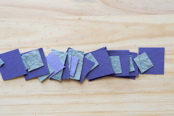 purple and gray textured paper tiles arranged in a row on a wood background
