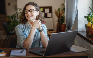 Happy creative young woman in eyeglasses working on laptop at home. Remote work, small business and freelancing concept