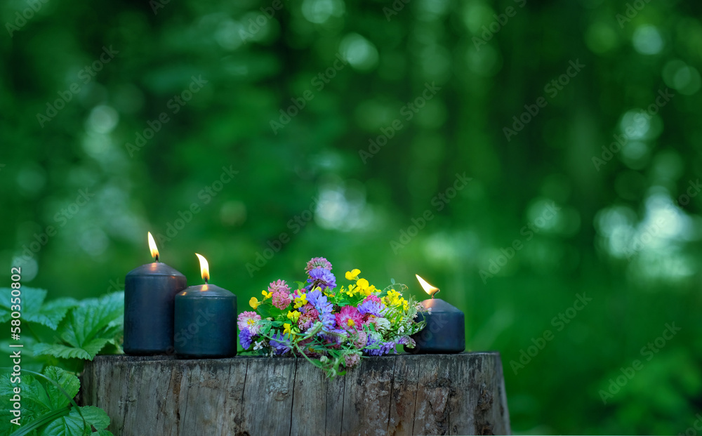 Wall mural magic candles and flowers on tree trunk in forest, green blurred natural background. wiccan practice