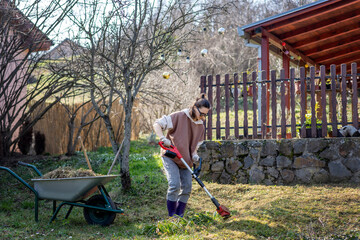 Spring garden work, cleansing the land. Young woman cleaning the lawn mowing the grass using a lawn...