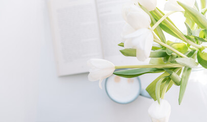 Bouquet of tulips with book and cup of coffee on white table.