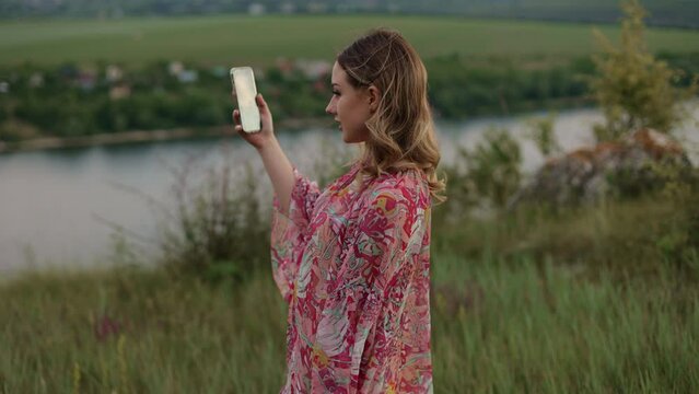 young pretty girl woman walks in nature in a place with incredible scenery and shoots video on smartphone, blogger, walk, beautiful place, countryside