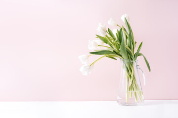 Bouquet of white tulips in glass decanter against pink background.