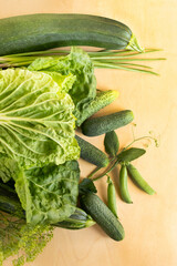 Vertical image of fresh natural green vegetables, Chinese cabbage, cucumbers, zucchini, peas in a craft paper bag on a wooden background