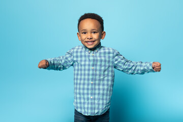 Portrait of adorable african american boy in casual clothes smiling at camera, standing over studio wall, free space