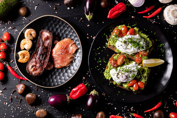 Avocado Toast with Poached Eggs and Seafood Platter on Dark Table.
Healthy avocado toast with poached eggs, cherry tomatoes, and chives, served alongside a seafood plate with salmon, octopus, and shri