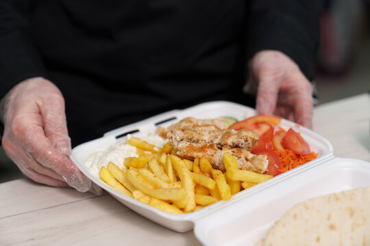 Cook packs grilled souvlaki meat, French fries and vegetables in lunch box for delivery. Traditional Greek fast food meal for dinner