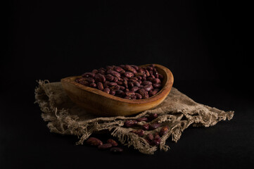 Red beans in a wooden plate on a black background.