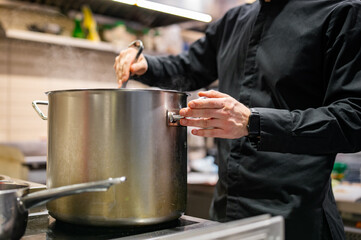 Fototapeta na wymiar chef pouring tasty soup from big pot into bowl on restaurant kitchen