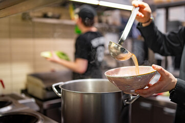 chef pouring tasty soup from big pot into bowl on restaurant kitchen