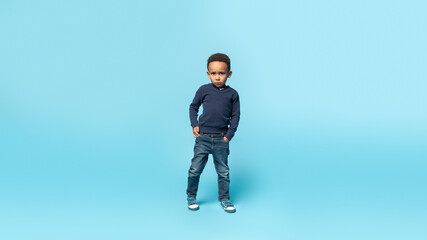 Naklejka premium African american child boy in casual wear standing with serious expression, holding hands in pocket, full length
