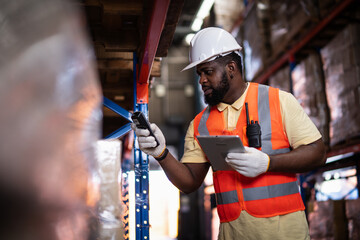 African American male warehouse worker scanning package with barcode scanner to count inventory balance in online system, holding tablet in hand for checking real time update in storage warehouse.