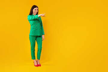 Happy stylish woman standing and pointing fingers at empty space, isolated on yellow background, full length, banner