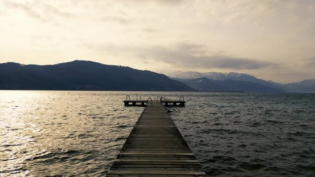 Beautiful low altitude drone view of Lake Attersee, Upper Austria, Europe, on a dark, cloudy, cold early spring day - camera moves along wooden footbridge, then ascends upwards 