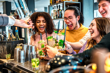Barman lady preparing cocktails - Multiracial friends cheering mojitos at counter bar restaurant -...