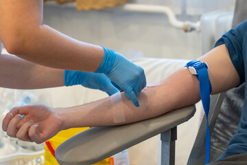 A nurse in blue gloves inserts a needle to take blood. Blood donation