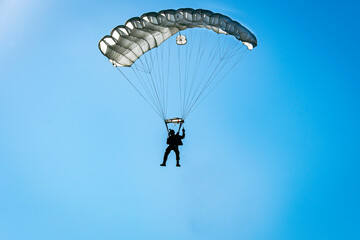 Silhouette of a parachutist descending with a white parachute