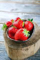 Ripe red strawberries from organic cultivation offered as a close-up in a rustic design bowl on old faded wood