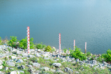 Staff gauge water at dam background. Four red water level gauge scale at lake - obrazy, fototapety, plakaty