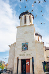 White small church temple in Bulgaria. Birds fly across blue sky. Inscription says: Church Rojdestvo Hristovo. High quality photo