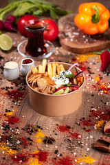 Doner Kebab Bowl with Chicken, Fries, and Fresh Vegetables.
Takeaway bowl filled with sliced grilled chicken doner, French fries, cucumber, tomato, lettuce, and red pepper. Styled on a rustic wooden t