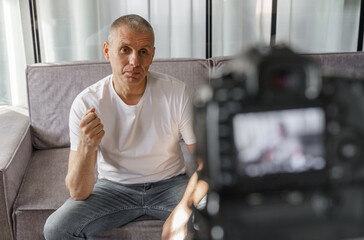 Confident successful man talking and recording vlog on camera in home interior.