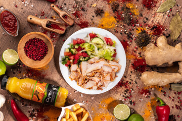 Doner Kebab Bowl with Chicken, Fries, and Fresh Vegetables.
Takeaway bowl filled with sliced grilled chicken doner, French fries, cucumber, tomato, lettuce, and red pepper. Styled on a rustic wooden t