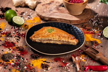 Slice of Traditional Baklava with Nuts on Black Plate and Rustic Background.
Golden slice of...