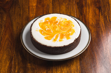 Cheesecake with orange mousse on a white plate with a golden edge on a wooden table.