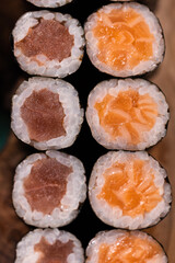 Assorted Salmon and Tuna Hosomaki Rolls with Soy Sauce on Wooden Plate.
Top-down view of assorted hosomaki sushi rolls with salmon and tuna, served with soy sauce, wasabi, ginger, and chopsticks on a 