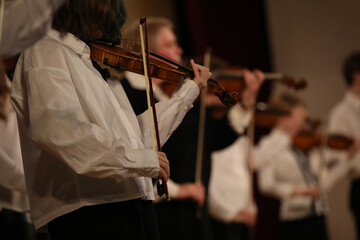 A group of musicians playing the violin standing in a row on a stage with musical instruments