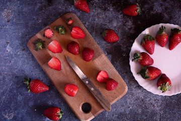 Cut strawberries on a wooden board with a knife.
