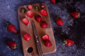 Cut strawberries on a wooden board with a knife.
