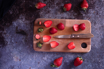 Cut strawberries on a wooden board with a knife.