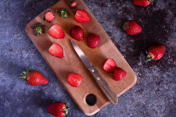 Cut strawberries on a wooden board with a knife.