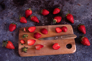 Cut strawberries on a wooden board with a knife.