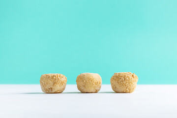 Three Sesame-Covered Balls on White and Turquoise Background. Minimalist composition of three sesame-covered balls (possibly rice balls or sweet treats) placed in a row on a clean white surface with

