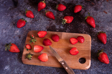 Cut strawberries on a wooden board with a knife.