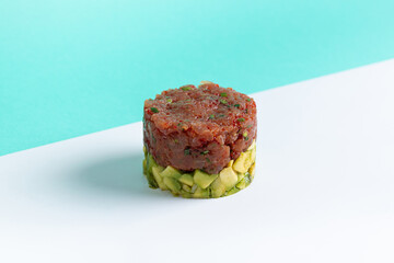 Tuna Tartare with Avocado on White and Turquoise Background. Minimalist gourmet tuna tartare layered over fresh avocado, styled in a round form on a clean white surface with a turquoise backdrop. Eleg
