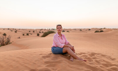 Fototapeta na wymiar European attractive woman sitting on the crest of a dune in desert