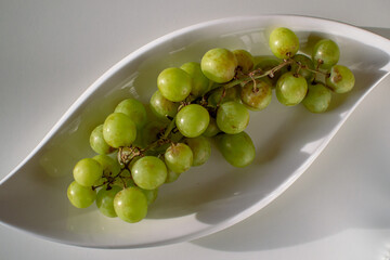 White plate filled with green grapes on a white table