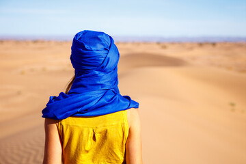 Traveler woman with blue turban looking at Sahara desert, sand sunes in Morocco