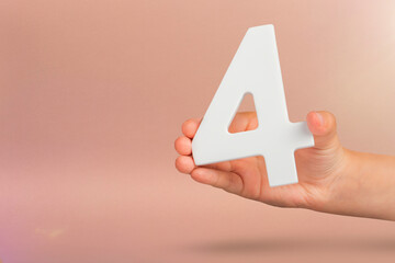 number four in hand. Hand holding white number 4 on red background with copy space. Concept with...