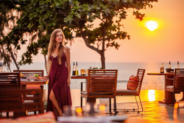 Elegant attractive smiling woman on romantic dinner in luxury gourmet restaurant. Sexy elegant girl in evening dress enjoying dinner date. Romantic sunset on the beach restaurant with sea view