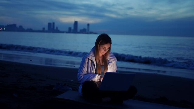 female freelancer is using a laptop on the beach of the sea in the evening