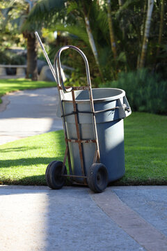 A large green waste container on a dollie so it can be moved easily. Yard work tools, garden clippings.