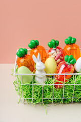 Baby Easter Basket gifts. Basket with Easter bunny, egges and carrots with sweets on pink background. Holidays decorations and gifts.
