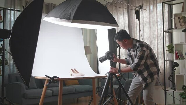 Asian Male Photographer Adjusting Position Of Women'S Shoes While Taking Photos Of Them In Home Studio 

