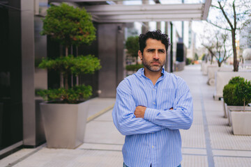Middle-aged Latin man with scowl and crossed arms in the city. Copy space.