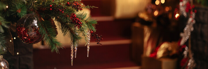 A branch of a xmas tree decorated with New Year and xmas toys the background of a bokeh of yellow and golden blurred lights of garlands. Banner for website header design with copy space.